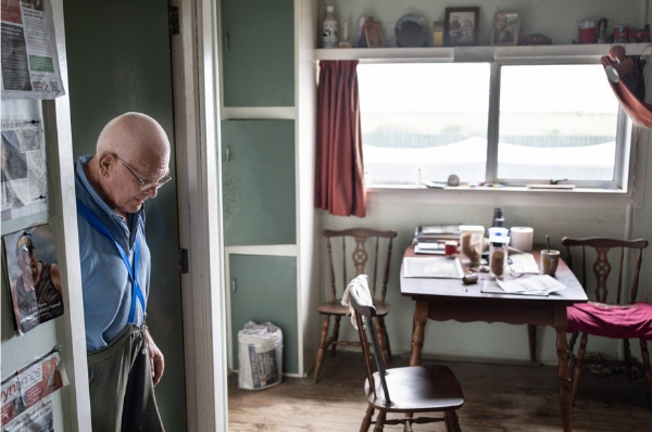 Elderly man walking through doorway of his dining room, looking down