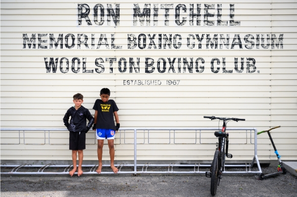 Two young boys standing in front of a Woolston Boxing Club sign