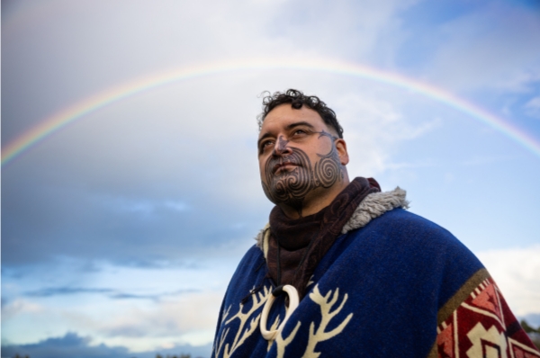 Man with facial tattoo standing in front of a rainbow